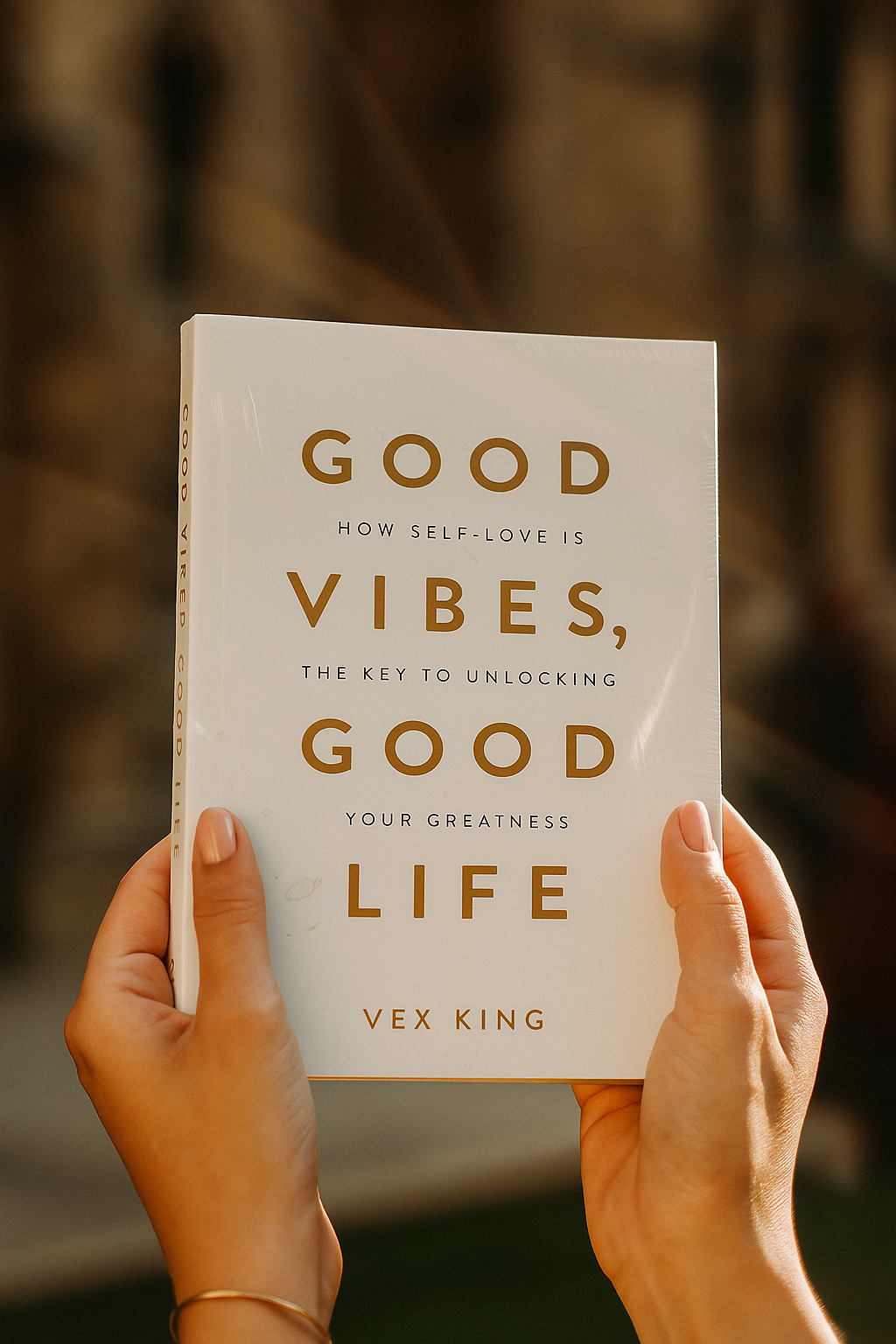 Book titled 'Good Vibes, Good Life' by Vex King held by hands against a blurred background